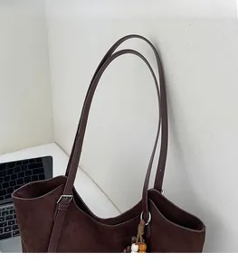 Détail du cabas en daim marron café avec lanières en cuir et pompon en perles de bois