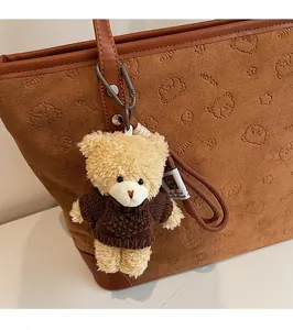 Close-up of a plush beige teddy bear charm in a brown knit sweater on a tote bag