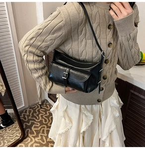 Detail of a black shiny shoulder bag with a silver buckle worn by a model in a beige sweater