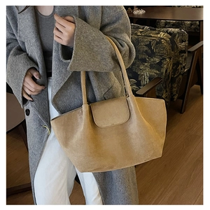 Lifestyle shot of a large light brown suede tote bag carried by a model in a cafe