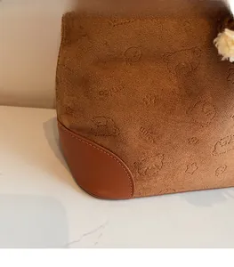 Detail of brown suede tote with cartoon bear embossing and dark leather corners