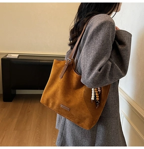 Détail du cabas en daim caramel avec bandoulière en cuir et pendentif en perles