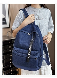 Detail of dark blue denim backpack featuring front zipper pocket and fashionbag strap