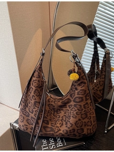 Fashionable leopard print shoulder bag with plush pom-poms and leather strap in soft lighting