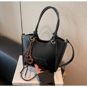 Detail of a matte black handbag with embossed lettering and a woven tassel charm