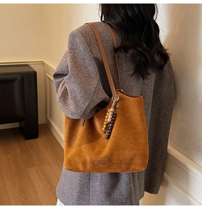 Détail d'un sac cabas en daim marron avec pendentif en perles de bois et logo gaufré