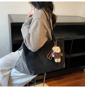 Black tote bag with star embossing and a cute bear plush pendant shown from the side