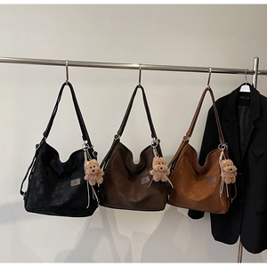 Close-up of three large faux suede tote bags in black and brown with plush bear charms