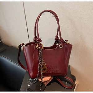 Detail of burgundy vintage tote bag featuring knotted handles and decorative wood pendant