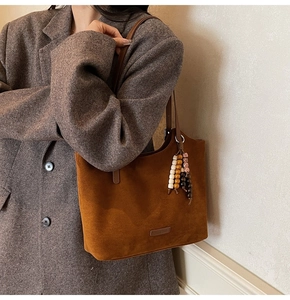 Détail d'un sac cabas en daim marron avec pompon perlé ethnique et écusson logo minimaliste