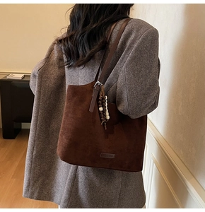 Détail du sac cabas en daim marron foncé avec pendentif en bois et écusson du logo