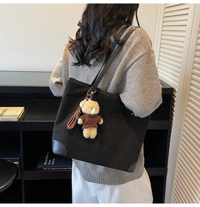 Detail of black tote bag with leather straps and a cute beige teddy bear charm accessory
