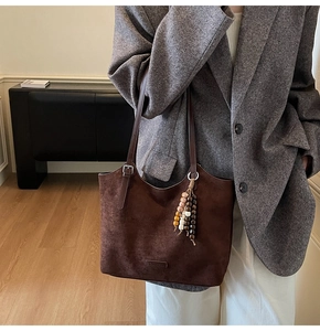Détail du sac cabas en daim marron avec gland de perles ethniques et logo en cuir cousu