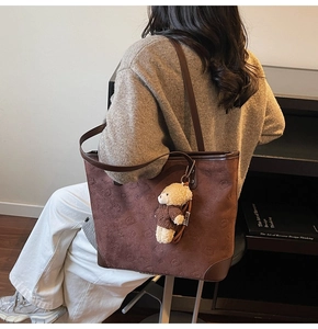 Detail of dark brown tote bag with embossed bear patterns and a cute plush bear pendant