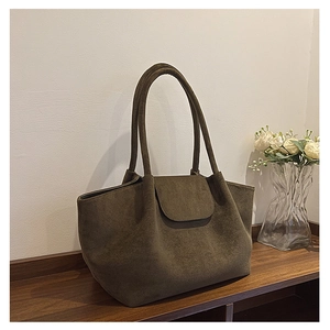 Detail of a large suede tote bag in dark green placed on a rustic wooden table