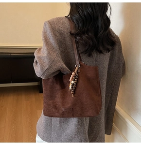 Détail d'un cabas en daim marron foncé avec breloque en perles sur un blazer gris