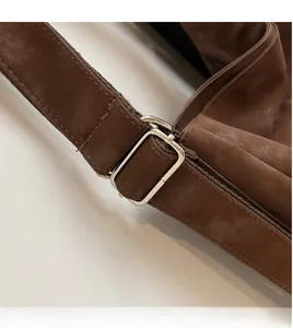 Detail of adjustable shoulder strap on brown suede bag with silver metal buckle