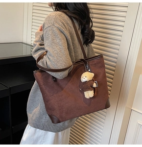 Detailed close-up of brown tote bag with bear embossing and plush charm on shoulder