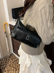 Minimalist black leather pillow bag worn as an underarm shoulder bag for stylish women
