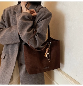 Gros plan détaillé du sac cabas en daim marron foncé avec breloque en bois et logo