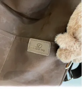 Close-up of deep brown suede tote with brand tag and plush side keychain accessory