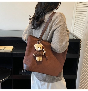 Detail of a large brown suede tote bag featuring a cute teddy bear charm and embossed bear pattern