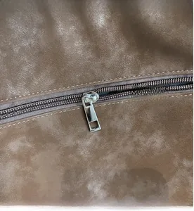 Close-up of a smooth silver metal zipper on a brown suede vintage tote bag texture