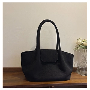Detail of a large black suede tote bag with a semicircular flap on a wooden surface
