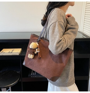 Detail of brown suede tote bag with embossed bear patterns and plush bear keychain