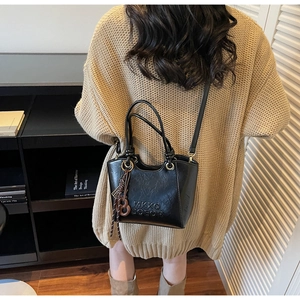Détail d'un sac à main en similicuir noir avec lettrage embossé et pendentif tissé