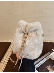 Plüschige beige Kunstfell-Beuteltasche mit braunem Kordelzug in der Hand gehalten