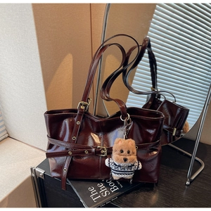 Détail d'un sac cabas marron foncé brillant avec boucles en métal et breloque ours en peluche