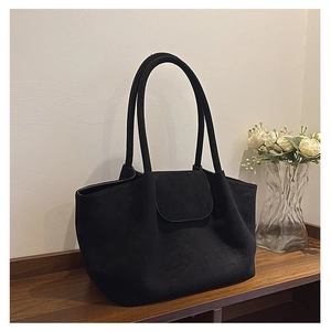 Detail of minimalist black suede tote bag with magnetic flap closure on wooden table