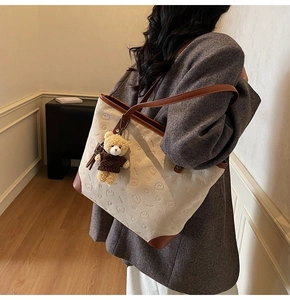 Detail of beige canvas tote bag with brown leather trim and cute bear plush charm