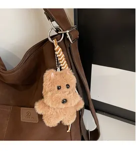Detailed view of a soft brown plush dog charm with metal hook on a leather tote bag