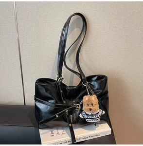 Détail d'un sac cabas en cuir ciré noir avec boucle dorée et breloque chien en peluche