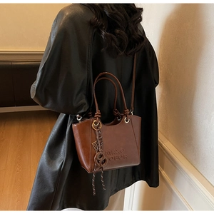 Detailed view of deep brown matte leather tote bag with embossed letters and ring charm
