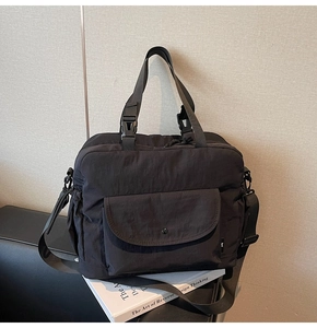 Detail view of black nylon tote bag featuring front flap pocket and sturdy buckle handles