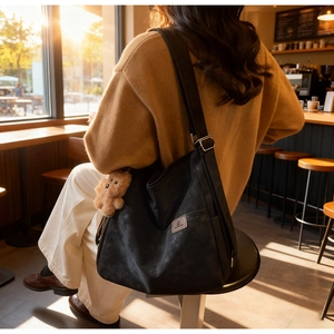 Detail of black matte tote bag with wide shoulder strap and brown teddy bear charm