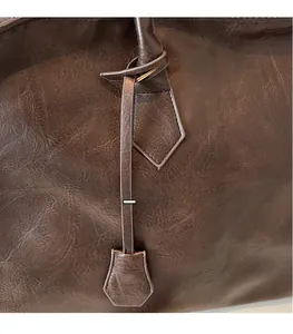 Détail du sac en cuir marron foncé montrant les coutures de l'anse et la texture cirée