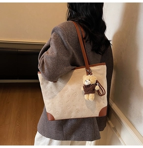 Detail of beige tote bag with bear patterns and plush charm on grey wool coat