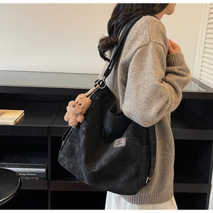 Detail view of large black matte tote bag with teddy bear charm and logo patch