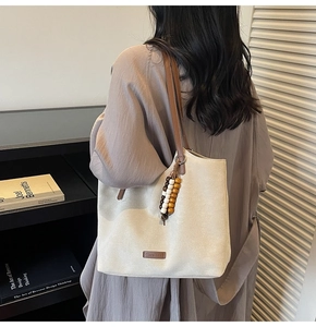 Détail du sac cabas en toile beige avec étiquette en cuir et breloque en perles de bois