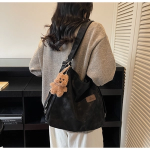Detailed back view of a large black tote bag with a plush bear charm on a female model
