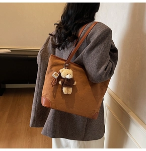 Detail of dark brown tote bag with bear embossing and plush charm on shoulder