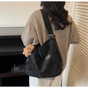Detail of black faux suede tote bag featuring silver buckle and cute plush bear charm