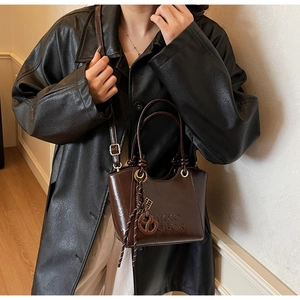 Close-up of deep brown glossy crossbody bag with embossed letters and stylish woven charm