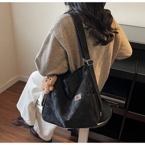 Detail of black large capacity shoulder bag with brown plush bear charm accessory