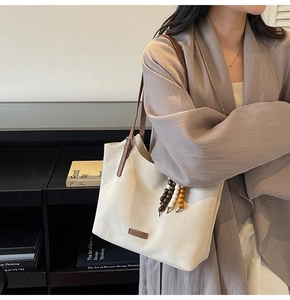 Détail du sac cabas beige avec bandoulière en cuir marron et pendentif en bois
