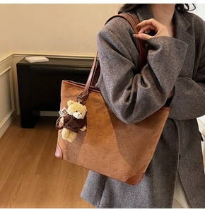 Close-up of brown tote bag with embossed bear patterns and a plush bear pendant charm